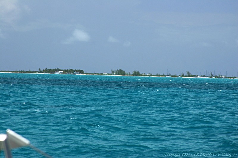 Anegada from one mile out through a telephoto lens. It is what you would see with a good pair of binoculars. The white roof at the left is Neptune's Treasure, which is the most important visual landmark for approaching the Anegada entrance channel. The red entrance buoy is now visible just to the left of Neptune's, just below the beach.