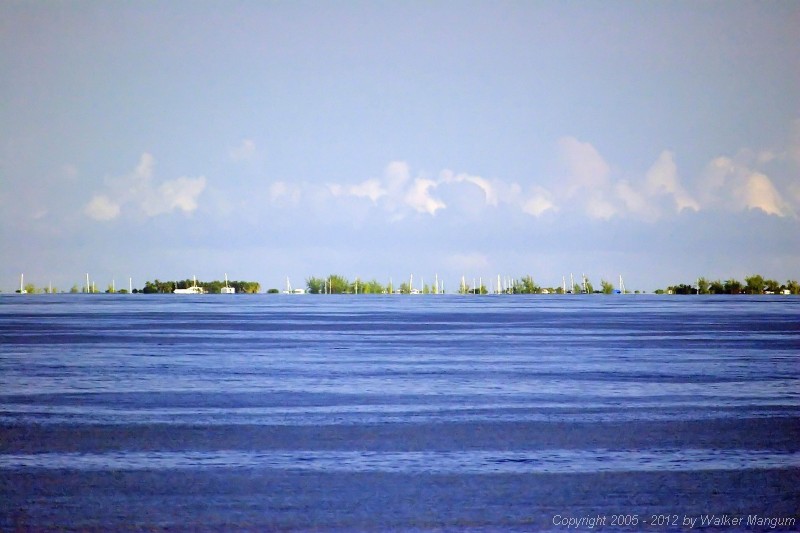 Anegada from 8 miles away, photographed from the top of the ferry with a long telephoto lens. Sailboats in the anchorage are still "hull down", with only their masts visible above the horizon. The buildings ashore have now appeared above the horizon.
