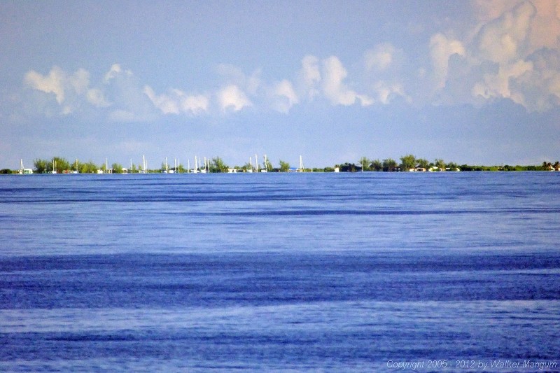 Anegada from 7 miles away, photographed from the top of the ferry with a long telephoto lens. Sailboats in the anchorage are only partially "hull down", with parts of their hulls still below the horizon. The buildings ashore have now appeared above the horizon.